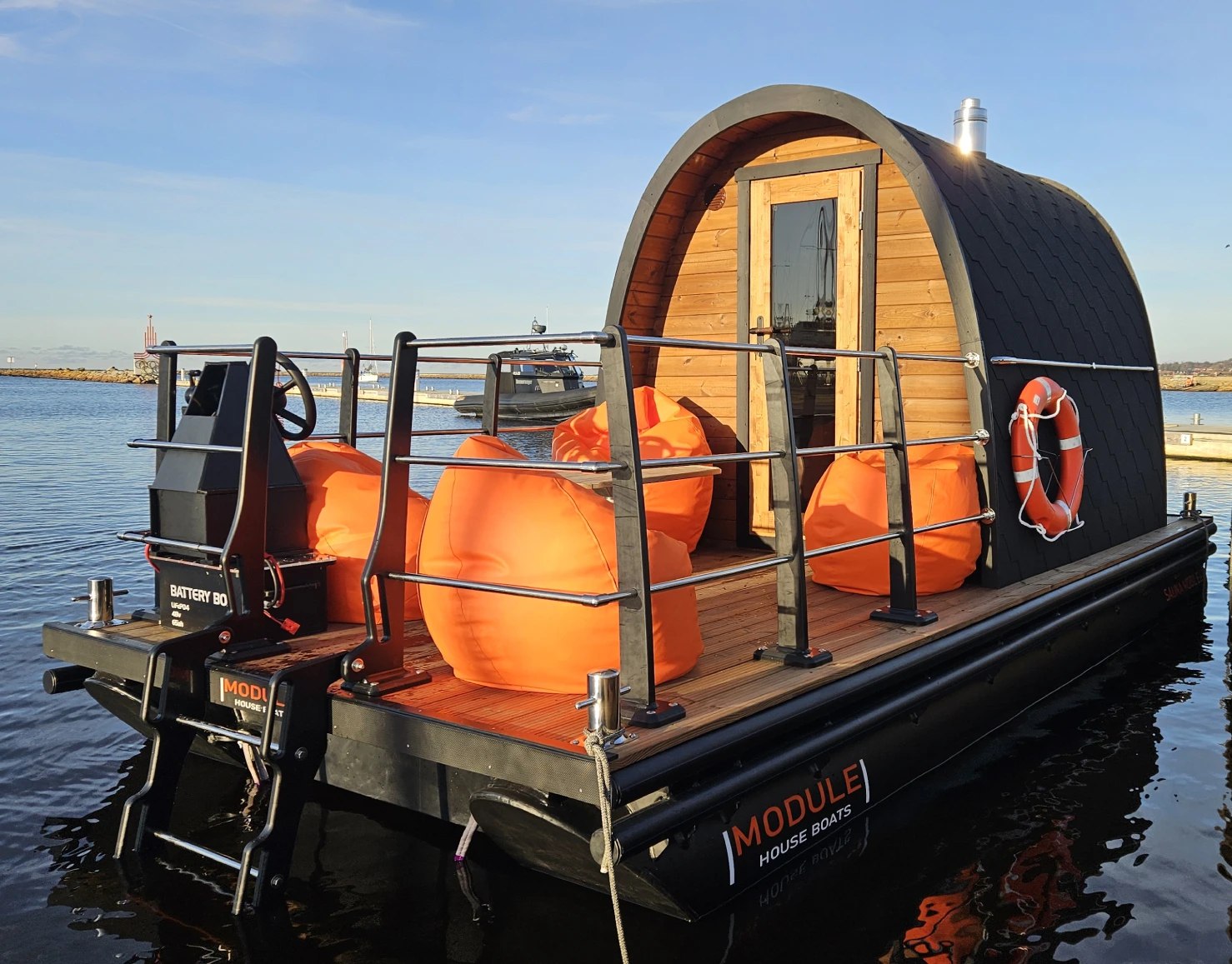Floating sauna is displayed. It is located in the sea. The floating foundation of the sauna is made from HDPE plastic modules. The decking is made from wood. The sauna itself is wooden as well. Manufactured in Estonia by MODULE HOUSE BOATS.